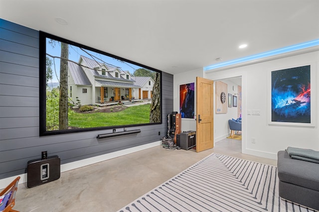 home theater room featuring concrete floors, baseboards, and wooden walls