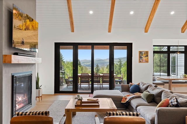 living area with a glass covered fireplace, a mountain view, recessed lighting, wood finished floors, and beamed ceiling