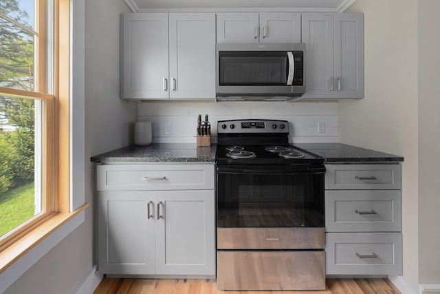 kitchen featuring appliances with stainless steel finishes, dark stone countertops, healthy amount of natural light, and light wood-type flooring
