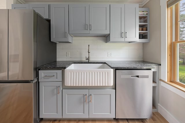 kitchen featuring stainless steel appliances, a sink, open shelves, dark stone countertops, and decorative backsplash