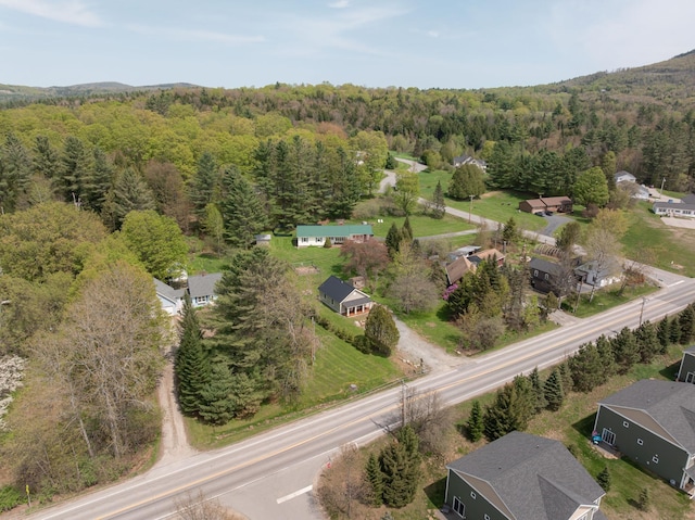 aerial view of property and surrounding area featuring a forest and nearby suburban area