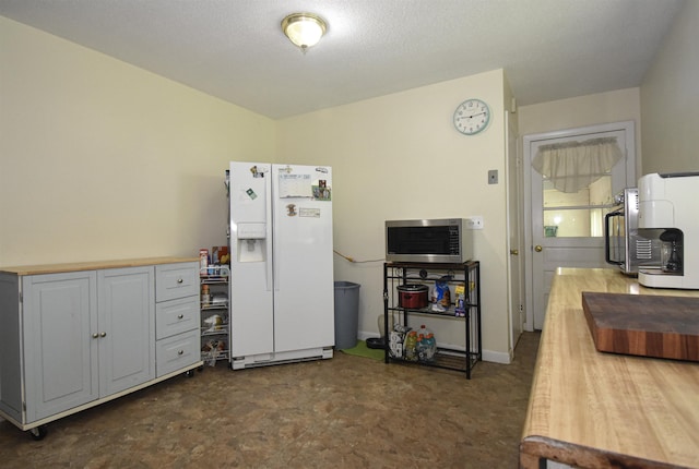 kitchen with white fridge with ice dispenser, stainless steel microwave, and butcher block counters