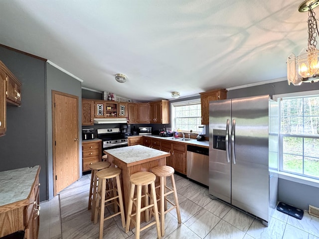 kitchen with stainless steel appliances, a sink, light countertops, a breakfast bar, and ornamental molding
