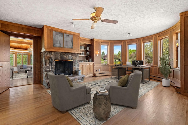 43 Sterling Pl, Bow, NH 03304 - living room featuring baseboard heating, light wood-style flooring, a fireplace, wooden walls, and a textured ceiling