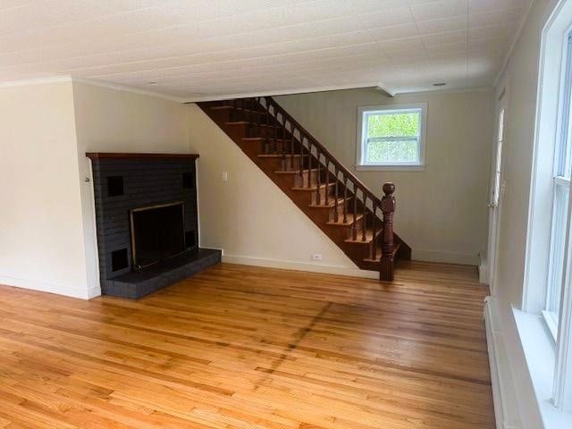 54 E Center St, Rutland City, VT 05701 - unfurnished living room with ornamental molding, stairs, light wood-style flooring, a brick fireplace, and baseboards