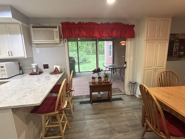 7 Juniper Ridge Rd, Exeter, NH 03833 - kitchen with a wall unit AC, white cabinets, white microwave, a breakfast bar, and dark wood-style flooring