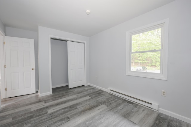 9 Winnisquam Shr, Tilton, NH 03276 - unfurnished bedroom featuring a baseboard heating unit, baseboards, wood finished floors, and a closet