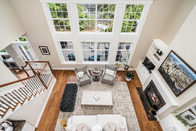 72 Settlers Ct, Bedford, NH 03110 - living room with wood finished floors, baseboards, a high ceiling, a glass covered fireplace, and stairway
