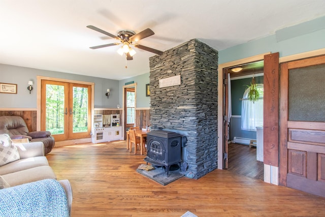 174 Andrews Rd, Holland, VT 05830 - living area with a baseboard heating unit, a wood stove, a wainscoted wall, wood finished floors, and a ceiling fan