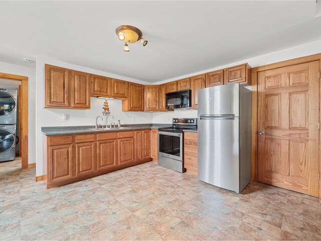 183 Morrie Rd, Washington, VT 05675 - kitchen featuring stainless steel appliances, a sink, stacked washer and clothes dryer, brown cabinetry, and dark countertops