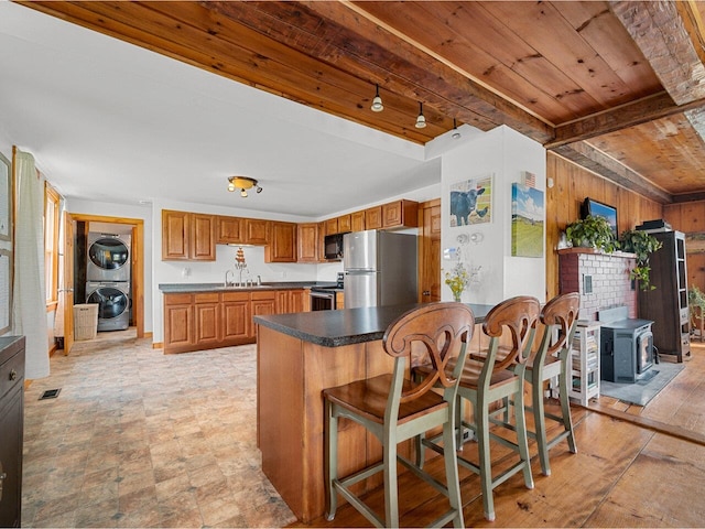 183 Morrie Rd, Washington, VT 05675 - kitchen with appliances with stainless steel finishes, stacked washer / dryer, wooden ceiling with exposed beams, brown cabinetry, and wooden walls