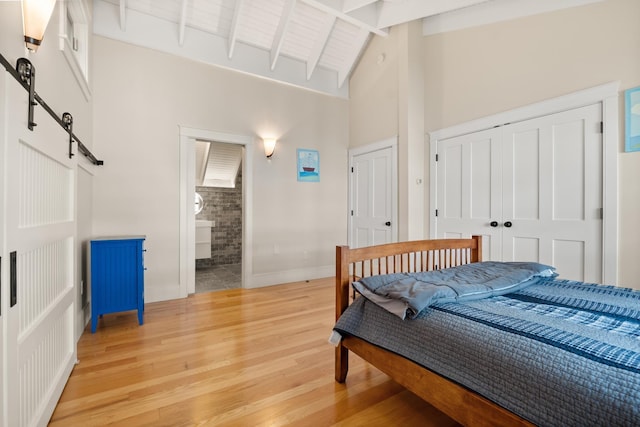 8 Wisteria Ln, Eliot, ME 03903 - bedroom featuring a barn door, light wood-style floors, beamed ceiling, high vaulted ceiling, and baseboards