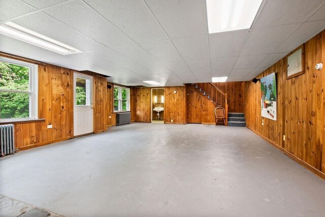 47 Dell Rd, Springfield, VT 05156 - unfurnished living room featuring concrete flooring, wooden walls, healthy amount of natural light, stairs, and radiator heating unit