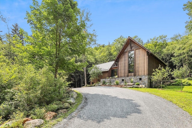 249 Falls Brook Ln, Stowe, VT 05672 - view of front of home with gravel driveway, stone siding, metal roof, a front yard, and a view of trees