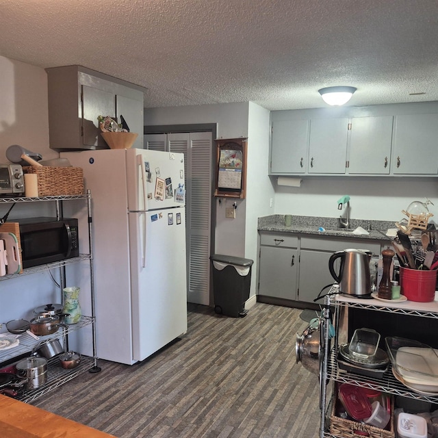 16 Oakwood Dr Unit 16, Claremont, NH 03743 - kitchen featuring black microwave, freestanding refrigerator, a sink, a textured ceiling, and dark wood-type flooring