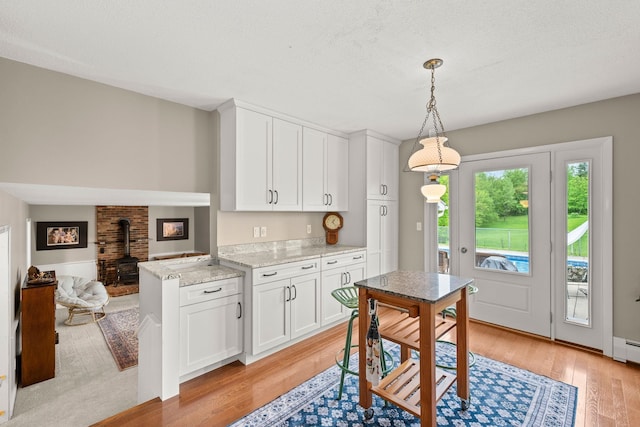 55 Honey Hill Rd, Hinesburg, VT 05461 - kitchen featuring light wood-style flooring, a wood stove, white cabinets, and pendant lighting