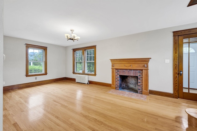 55 Washington St, Rochester, NH 03867 - unfurnished living room with radiator, wood finished floors, a chandelier, a brick fireplace, and baseboards
