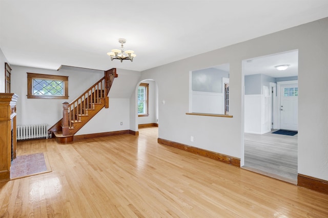 55 Washington St, Rochester, NH 03867 - unfurnished living room with radiator heating unit, light wood-type flooring, arched walkways, stairway, and healthy amount of natural light