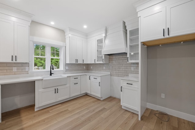 280 Sterling Dr, Laconia, NH 03246 - kitchen with a sink, custom range hood, backsplash, light wood-style flooring, and glass insert cabinets