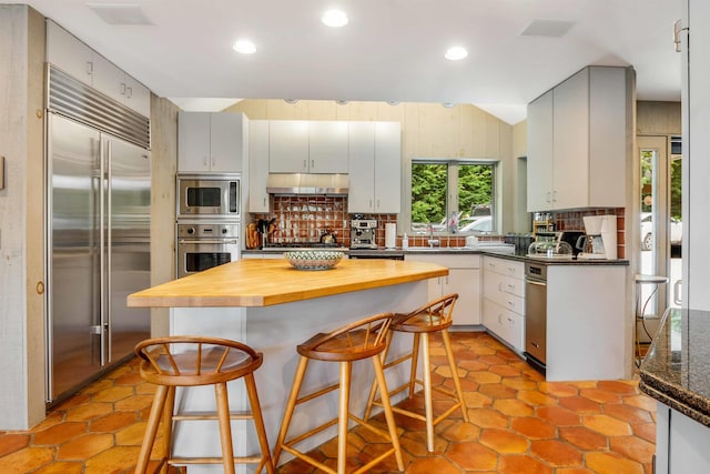 75 Westwood Rd, Sunapee, NH 03782 - kitchen featuring built in appliances, tasteful backsplash, under cabinet range hood, wooden counters, and a breakfast bar area
