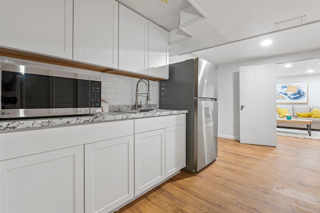 65 Sanborn St, Laconia, NH 03246 - kitchen featuring appliances with stainless steel finishes, a sink, light wood-type flooring, decorative backsplash, and white cabinetry