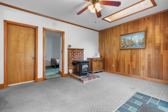28 Joslin Rd, Swanzey, NH 03431 - carpeted living room with a wood stove, a ceiling fan, ornamental molding, wood walls, and a skylight
