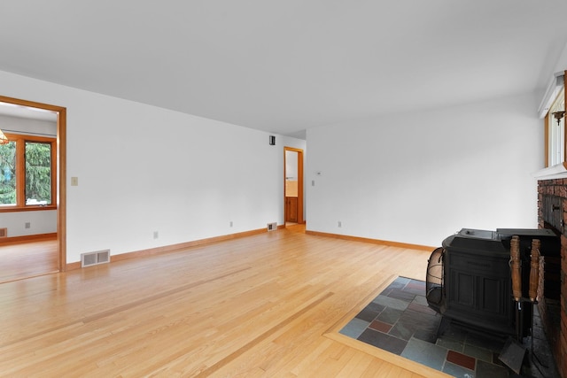 33 Wildwood Dr, Burlington, VT 05408 - unfurnished living room featuring wood finished floors, a brick fireplace, a wood stove, and baseboards