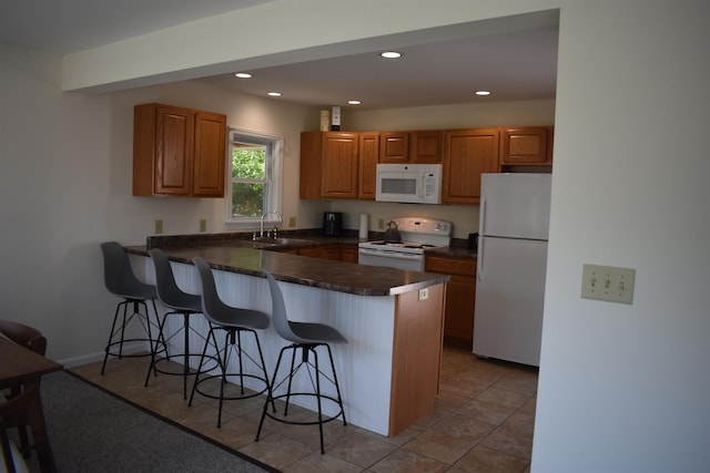 11 Creighton St, Newmarket, NH 03857 - kitchen featuring white appliances, a peninsula, a breakfast bar, a sink, and dark countertops