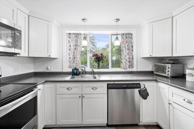 19 Overland St, Laconia, NH 03246 - kitchen featuring appliances with stainless steel finishes, a sink, white cabinets, dark countertops, and hanging light fixtures