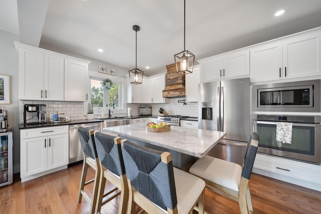 218 Manchester St, Nashua, NH 03064 - kitchen with appliances with stainless steel finishes, a sink, backsplash, a kitchen bar, and wood finished floors