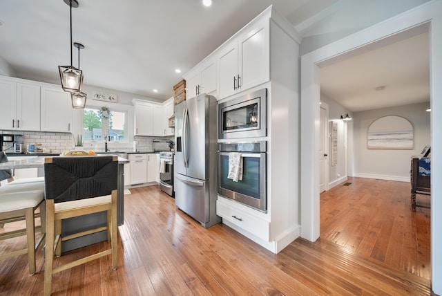218 Manchester St, Nashua, NH 03064 - kitchen with appliances with stainless steel finishes, decorative backsplash, light wood-style flooring, white cabinetry, and pendant lighting