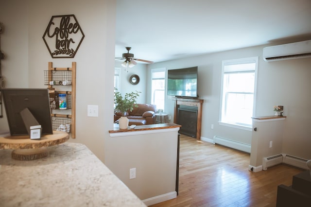 7 Plum St, Concord, NH 03301 - kitchen with a wall mounted AC, a baseboard radiator, light wood-style flooring, a glass covered fireplace, and ceiling fan