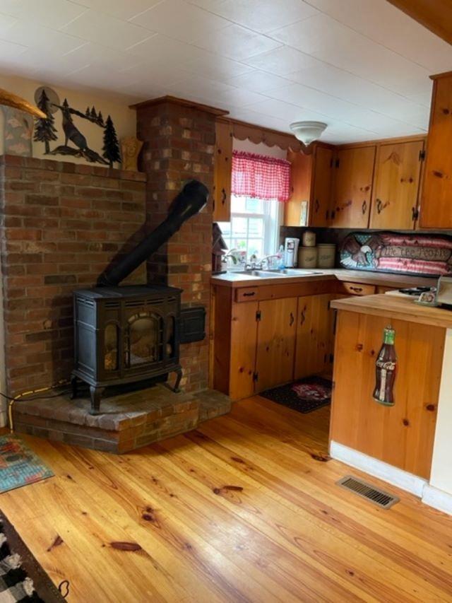 1295 Newark Pond Rd, Newark, VT 05871 - kitchen featuring a sink, light countertops, light wood-style flooring, and a wood stove