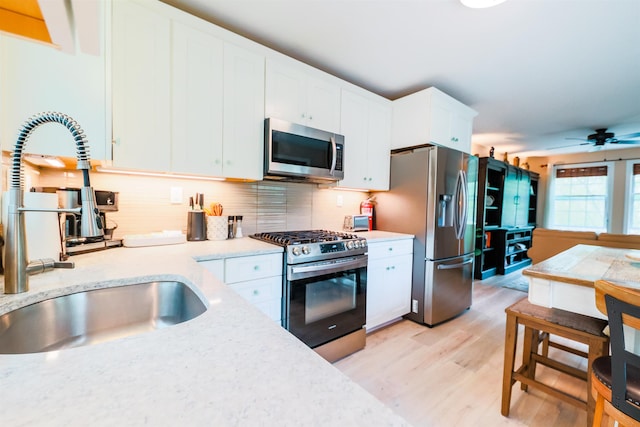 107 Artist Falls Rd, Conway, NH 03860 - kitchen featuring appliances with stainless steel finishes, a sink, light wood-style floors, white cabinetry, and decorative backsplash