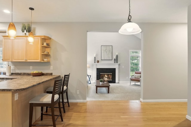 9 Swenson Rd, Bedford, NH 03110 - kitchen featuring light brown cabinetry, dark countertops, a kitchen breakfast bar, light wood-style floors, and baseboards