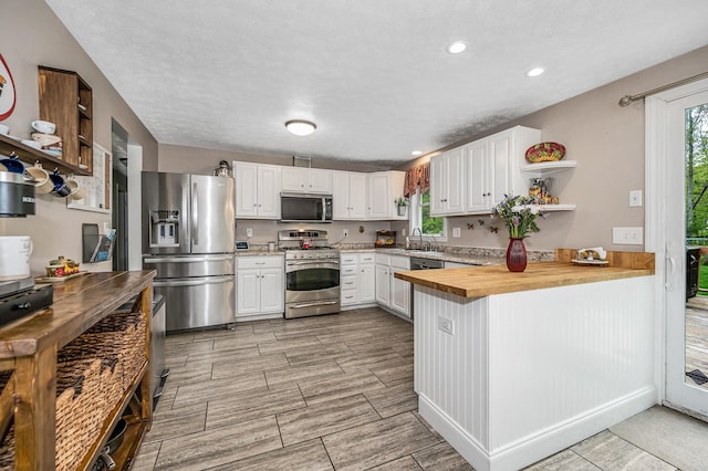 28 Hardy Rd, Londonderry, NH 03053 - kitchen featuring appliances with stainless steel finishes, butcher block counters, open shelves, a sink, and a peninsula