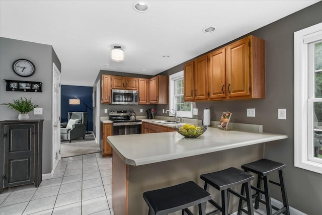 37 Level St, Merrimack, NH 03054 - kitchen with appliances with stainless steel finishes, a sink, brown cabinets, a peninsula, and a kitchen bar