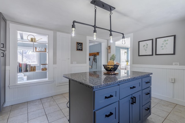 12 Harvard St, Exeter, NH 03862 - kitchen featuring light tile patterned floors, a wainscoted wall, dark stone countertops, blue cabinets, and a kitchen island