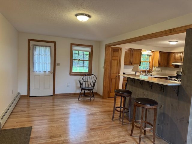 52 Jericho Rd, Grantham, NH 03753 - kitchen with baseboard heating, a breakfast bar area, stainless steel gas range, brown cabinetry, and light wood-style floors