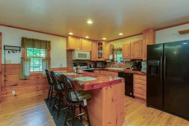 101 Mudgett Hill Rd, Loudon, NH 03307 - kitchen featuring black appliances, a breakfast bar area, a wainscoted wall, light wood-style floors, and glass insert cabinets