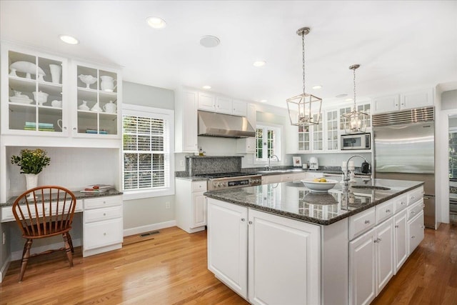 373 Whitford St, Manchester, NH 03104 - kitchen featuring under cabinet range hood, built in appliances, a sink, white cabinets, and a kitchen island with sink