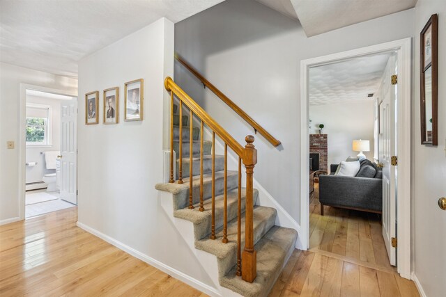 24 Theresa Ave, Salem, NH 03079 - stairs with a baseboard radiator, wood-type flooring, a brick fireplace, and baseboards
