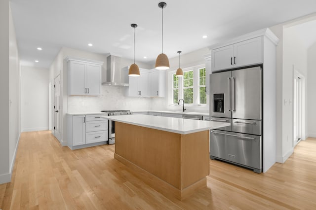 93 Stage Rd, Hampstead, NH 03841 - kitchen featuring appliances with stainless steel finishes, wall chimney range hood, light wood-style flooring, backsplash, and a center island