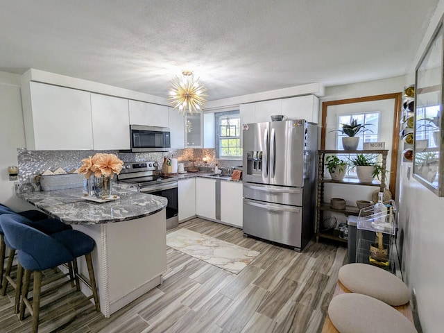 19 Bradford Dr, Salem, NH 03079 - kitchen featuring stainless steel appliances, a peninsula, white cabinetry, backsplash, and light wood-type flooring