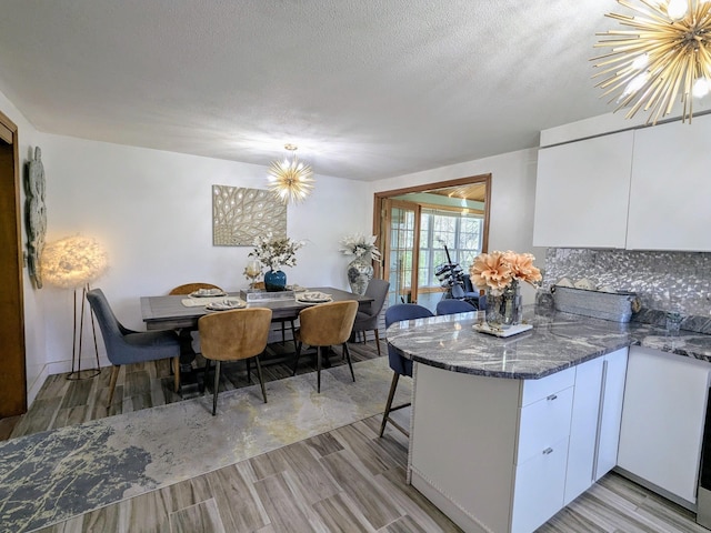 19 Bradford Dr, Salem, NH 03079 - kitchen with white cabinetry, a peninsula, light wood-style floors, dark stone counters, and a chandelier