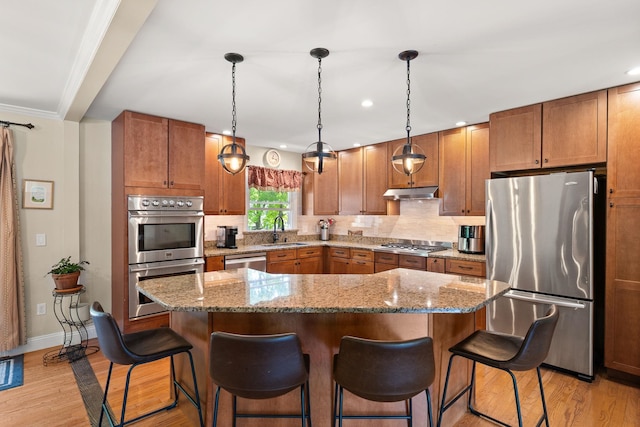 165 Tanglewood Dr, Colchester, VT 05546 - kitchen featuring stainless steel appliances, under cabinet range hood, a sink, light wood finished floors, and a kitchen breakfast bar