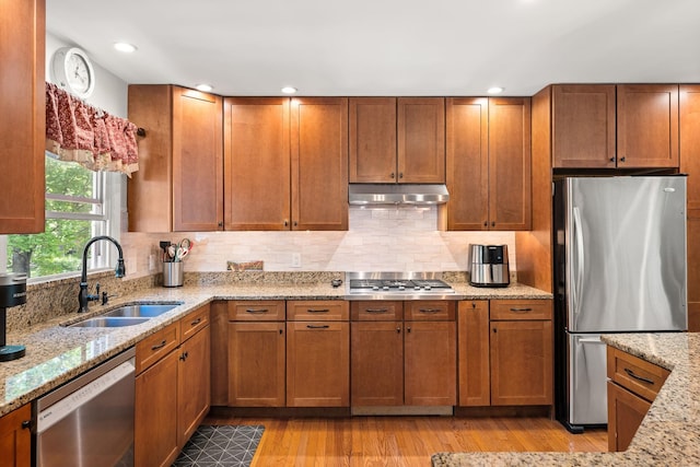 165 Tanglewood Dr, Colchester, VT 05546 - kitchen featuring stainless steel appliances, a sink, under cabinet range hood, light wood-style floors, and brown cabinetry