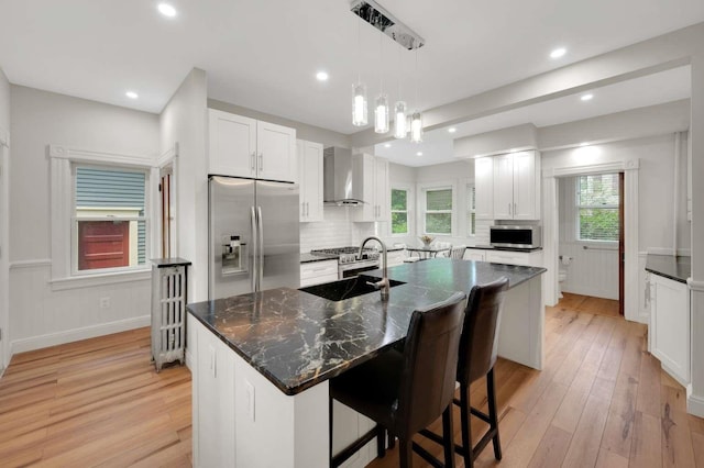 162 Sagamore St, Manchester, NH 03104 - kitchen with appliances with stainless steel finishes, wall chimney range hood, a sink, light wood-type flooring, and a kitchen island with sink