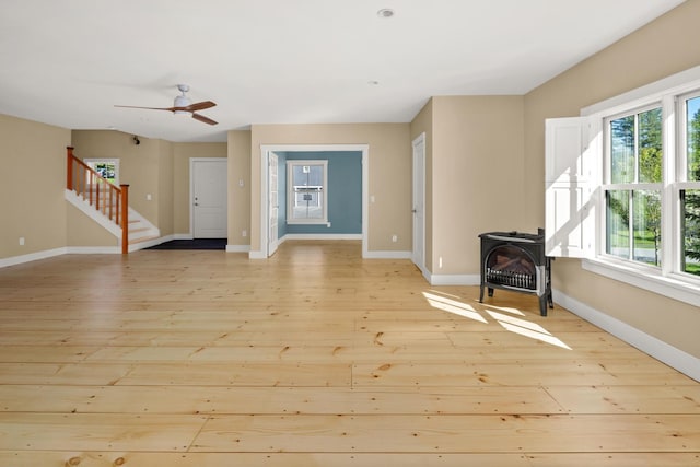 456 Thomas Ln, Stowe, VT 05672 - unfurnished living room featuring a wood stove, light wood-style floors, stairs, baseboards, and a ceiling fan