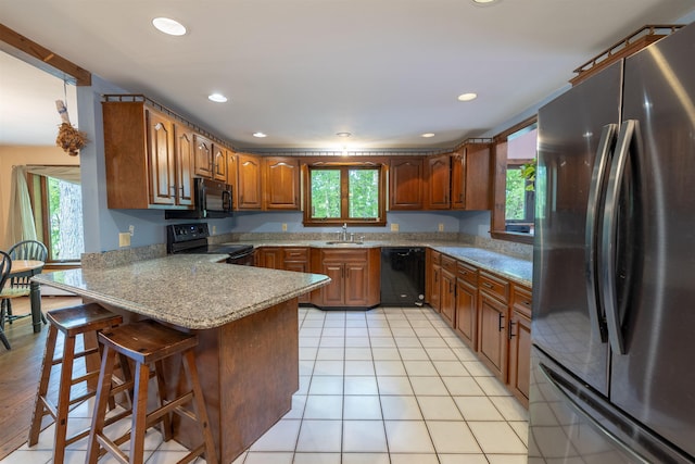 16 Berkeley St, Pelham, NH 03076 - kitchen with black appliances, a peninsula, a sink, a breakfast bar, and brown cabinetry